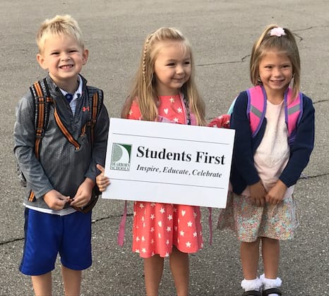 Three young students holding sign that says Students First: Inspire, Educate, Celebrate