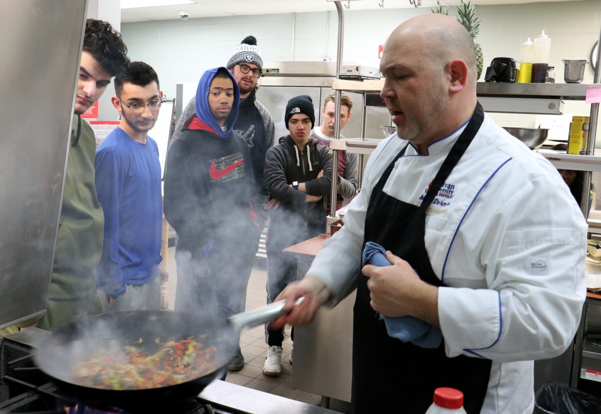 A chef shakes a skillet while six students watch at the Michael Berry Career Center.