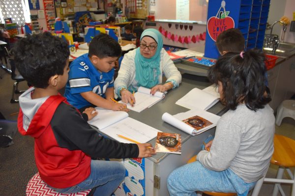 A teacher works on a lesson with a small group of students at a table.