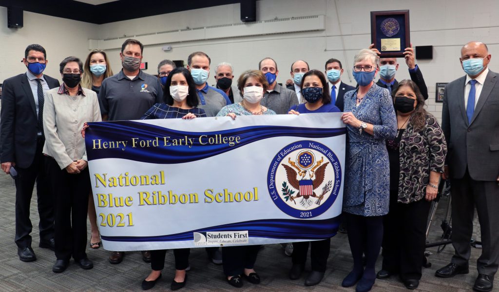 Posing with a sign celebrating Henry Ford Early College receiving a 2021 National Blue Ribbon Schools Award is a group of people including Board of Education members, school staff and Director Majed Fadlallah and Superintendent Glenn Maleyko.