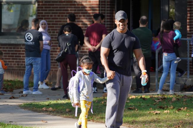 A man smiles while walking and holding a young girl's hand outside Haigh Elementary School during the fall of 2021.
