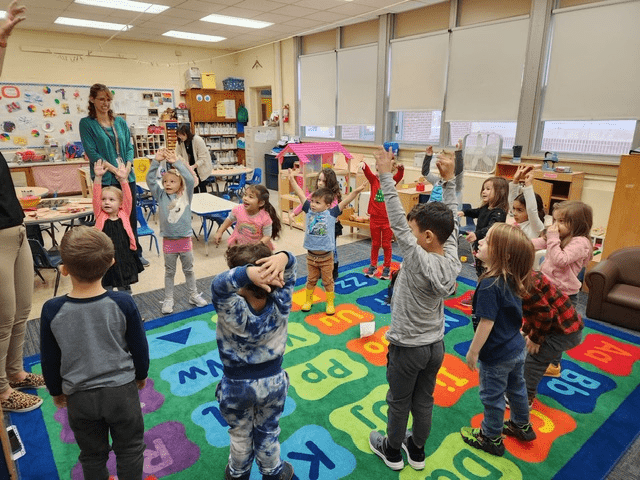 Young students stand and stretch in a classroom.