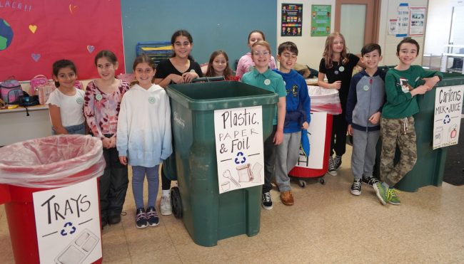 Eleven students pose by recycling containers for different types of school lunch waste.