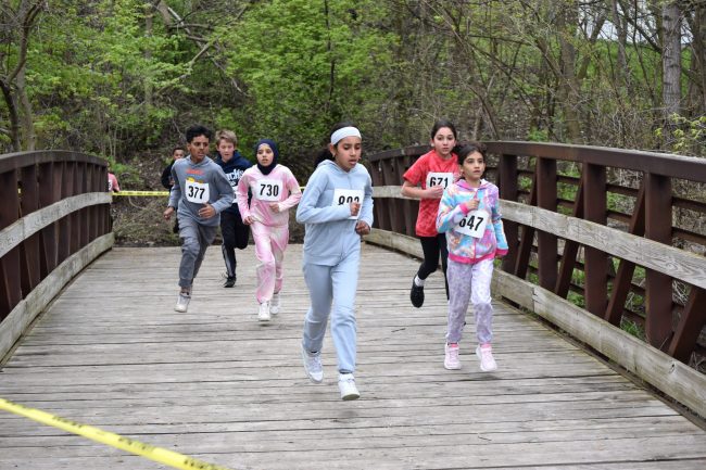 Elementary students race across a bridge at Ford Field Park during the 2023 Cipriano Memorial Cross Country Meet.