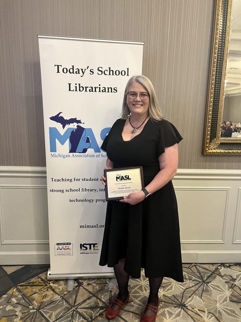 Nichole Alward holds her Michigan School Librarian of the Year Award near a sign for the awards dinner.