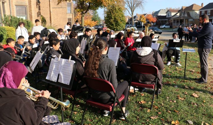 A school band performs on the school lawn on a sunny day.