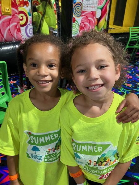 Two children smile while wearing bright yellow-green Summer Adventure Club shirts