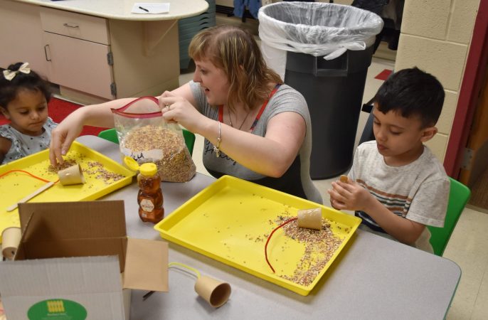 A teacher works with two young children on a craft.