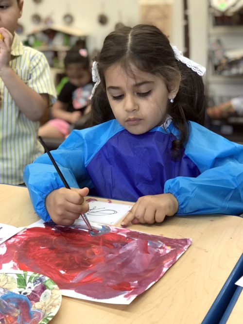 A young girl paints while sitting at a table.