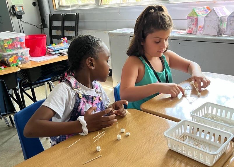 Two students work on creating a structure with toothpicks and mini marshmallows
