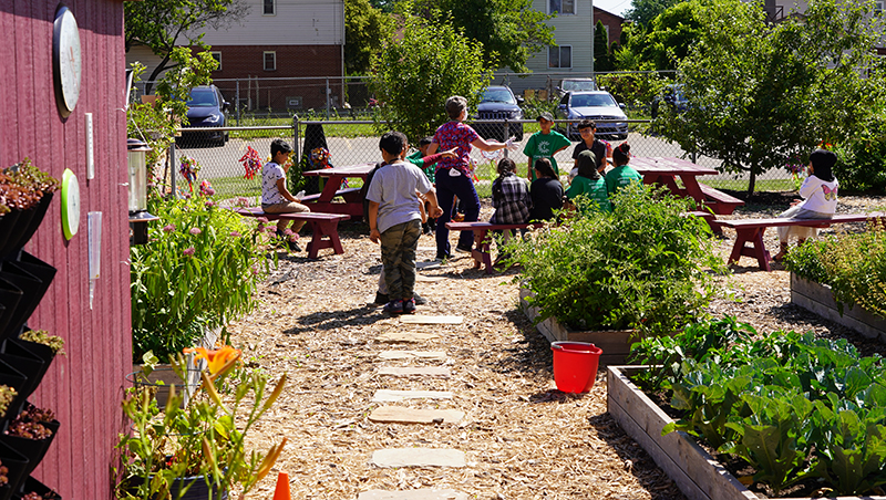 A teacher instructs students sitting on benches in a garden