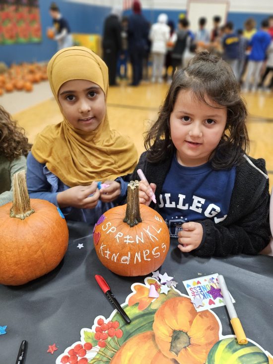 Two girls paint pumpkins to say Sprinkle Kindness