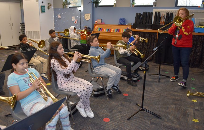 A group of students play trombones and trumpets with their teacher.