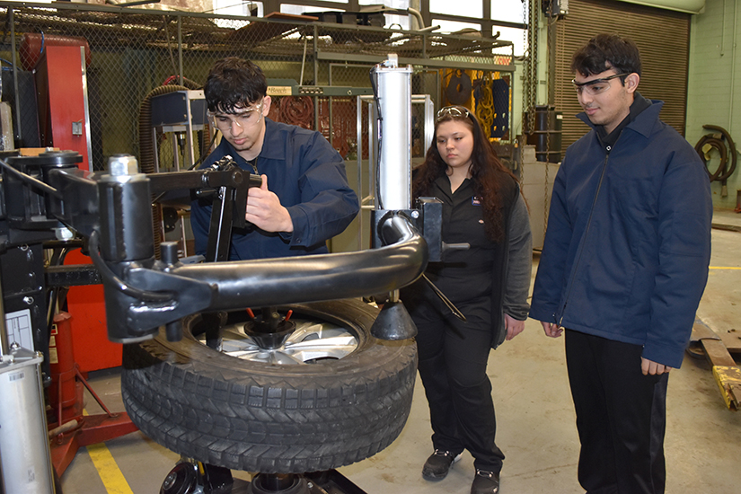 A Fordson High student works a tire changing machine while two other students watch.