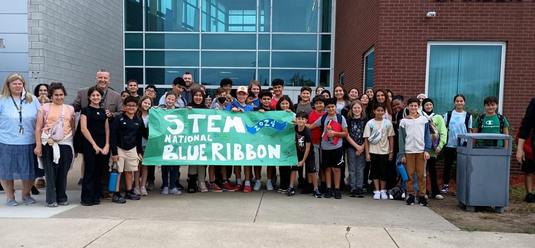 A group of students and staff stand with a banner saying STEM 2024 National Blue Ribbon School
