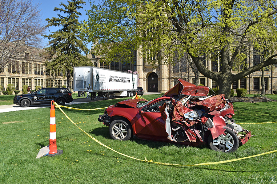 A severely wrecked car is shown in front of a semi holding driving simulators outside of Fordson High.