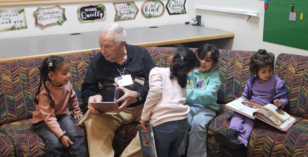Jim Martin sits on a couch reading to young students.