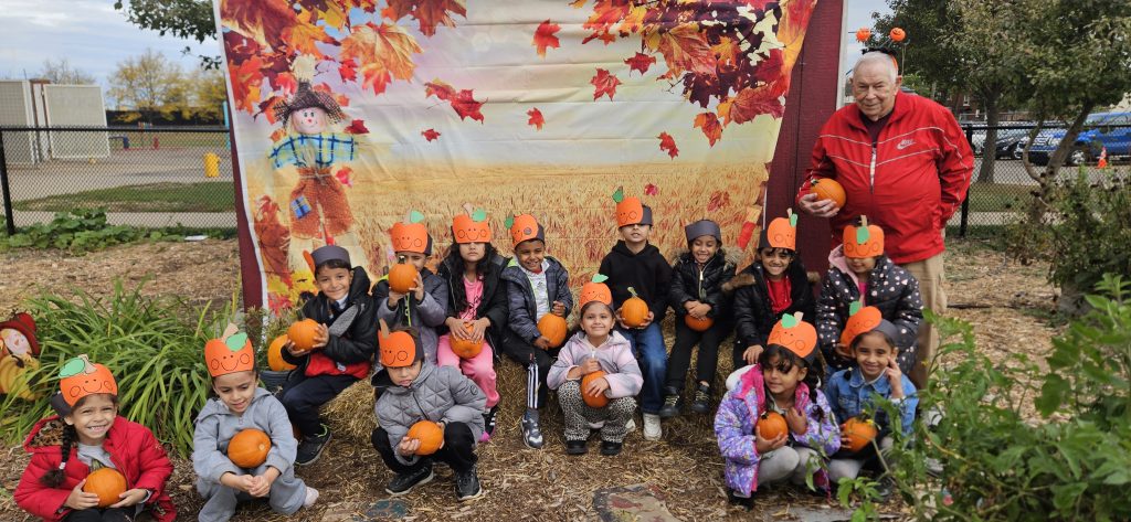 Students pose with pumpkins with Mr. Jim in front of a fall backdrop.