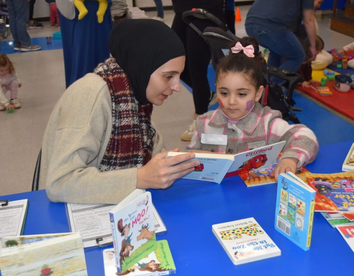 A woman reads a board book to a young child at a group event.