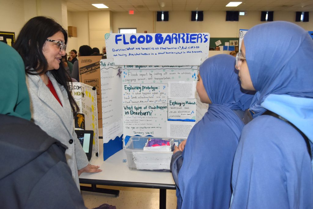 U.S. Rep. Rashida Tlaib talk to two students in front of their display on flood barriers.