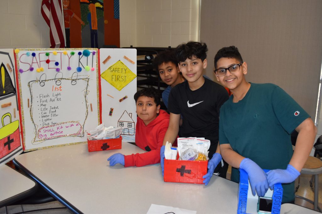 A group of students stand next to their display on first aid safety kits.
