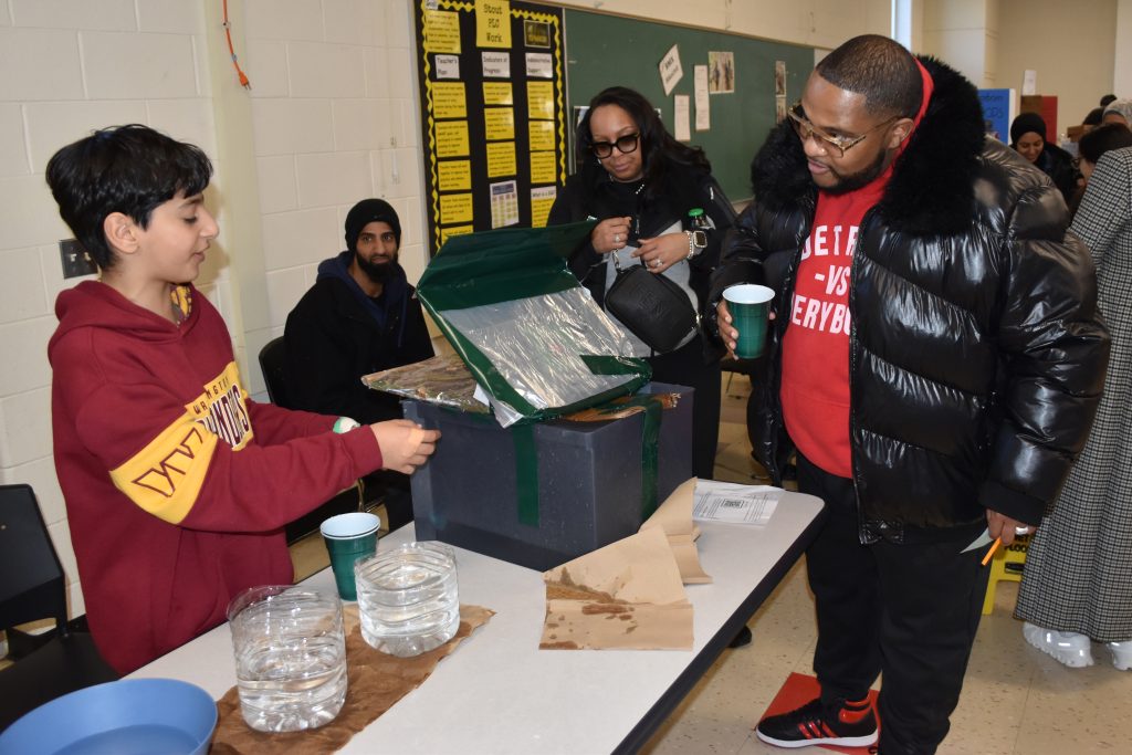 An adult pours water on a student display during the Stout flood information fair.