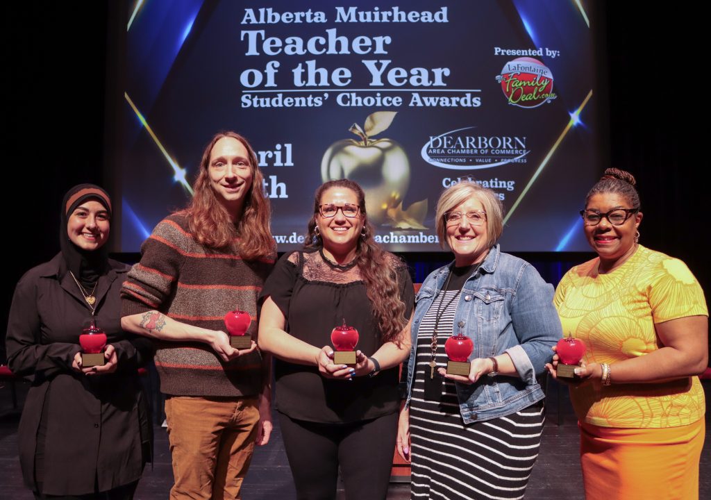 Five people stand on stage holding glass apple awards.