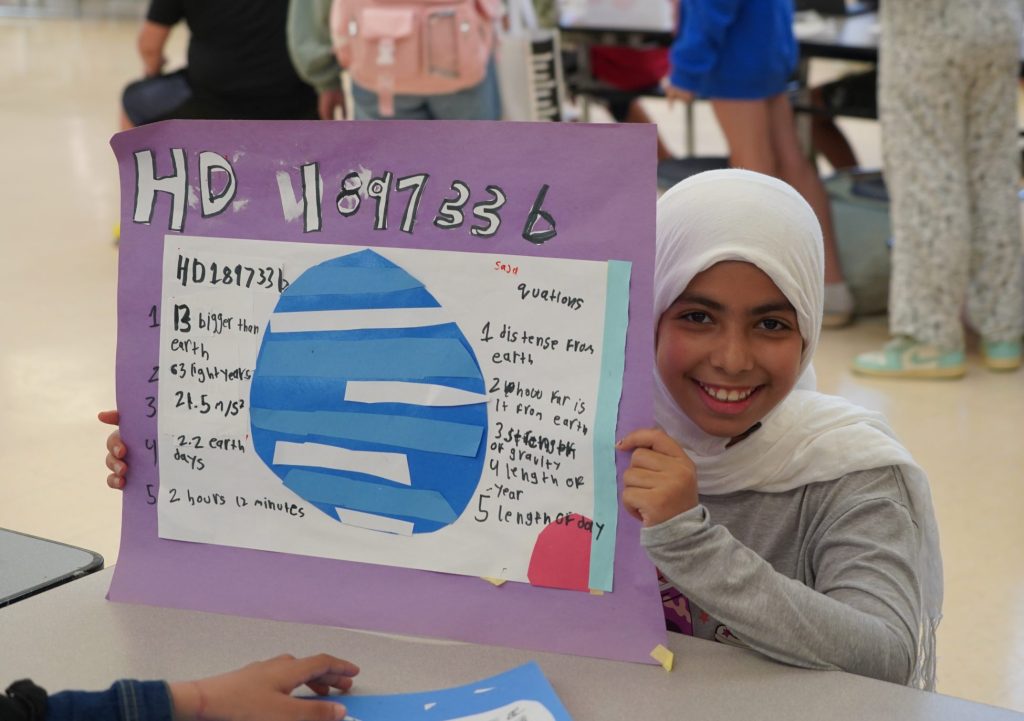 A student shows off a poster about a planet