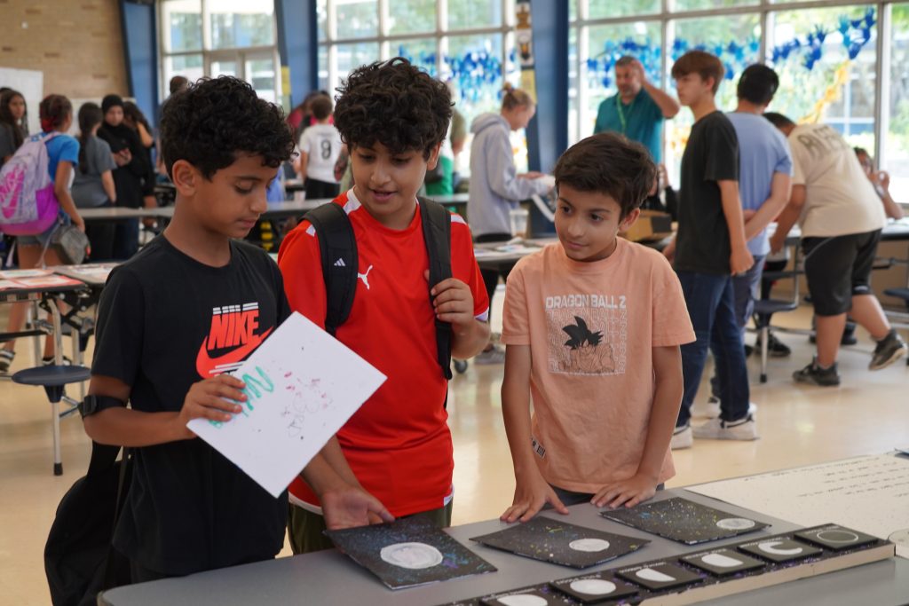 Three students look over pictures of the phases of the moon.