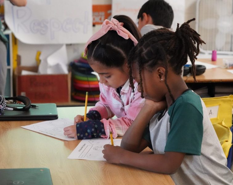 Two young students work at their desk